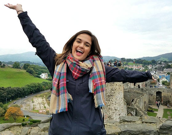 Student standing on a hill overlooking a field with arms spread open