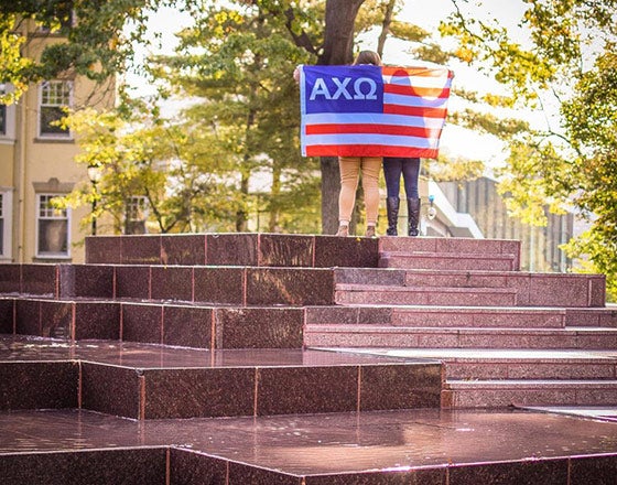 gl-8 Sorority sister with flag posing on a fountain on campus