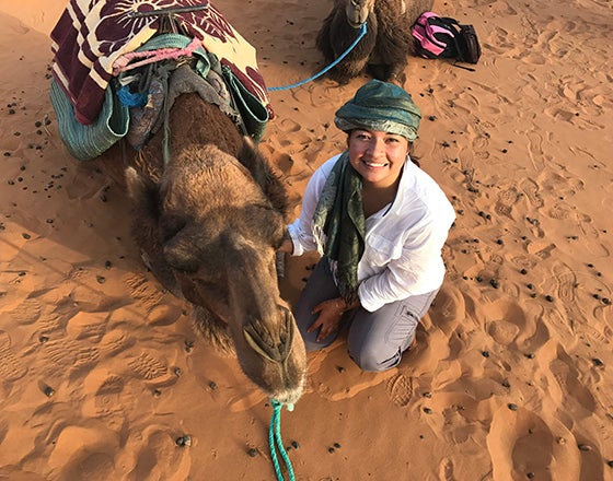 Student smiling next to a camel in the desert