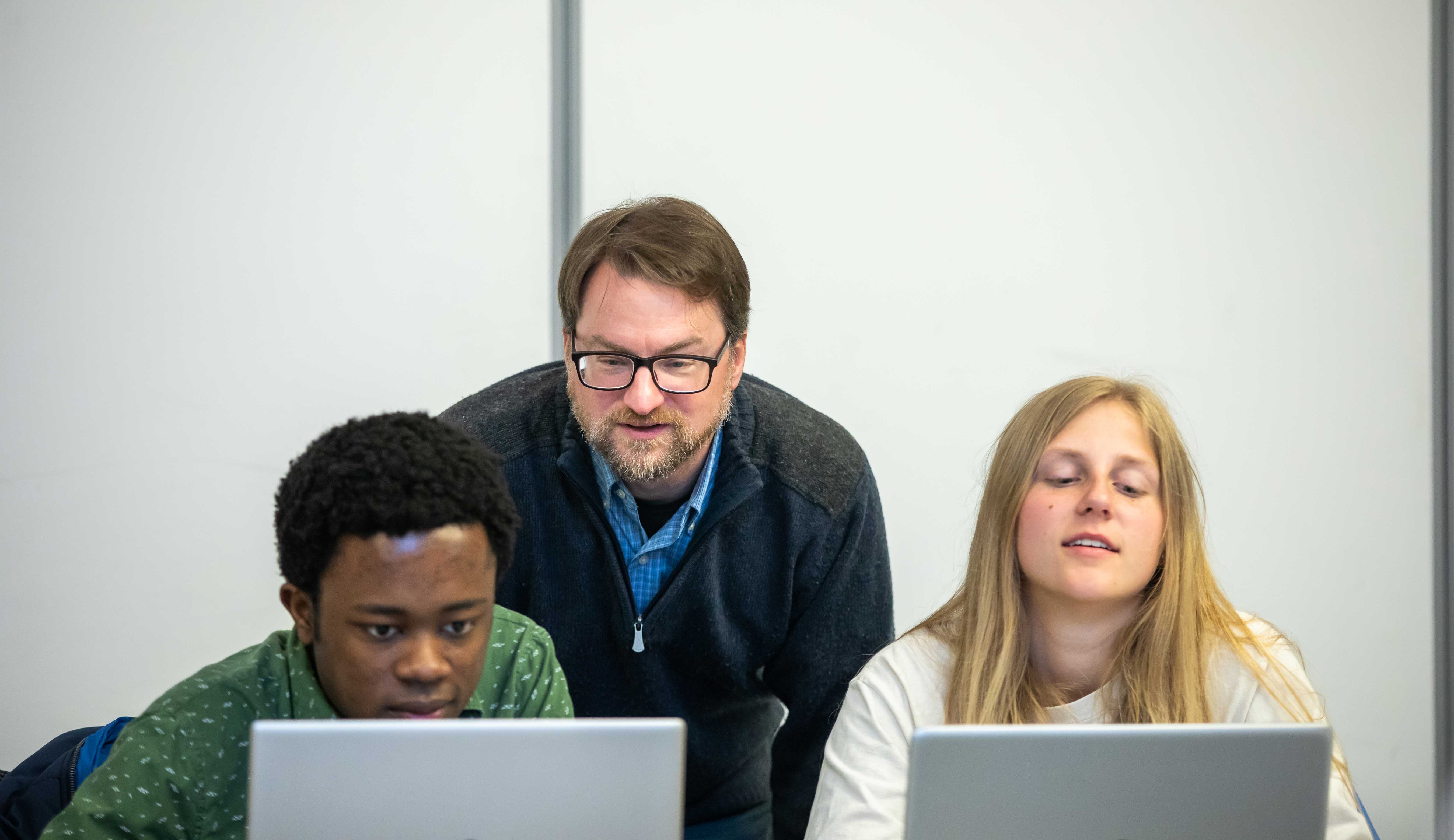Two students working on computers inside with a faculty member looking at the screen with them