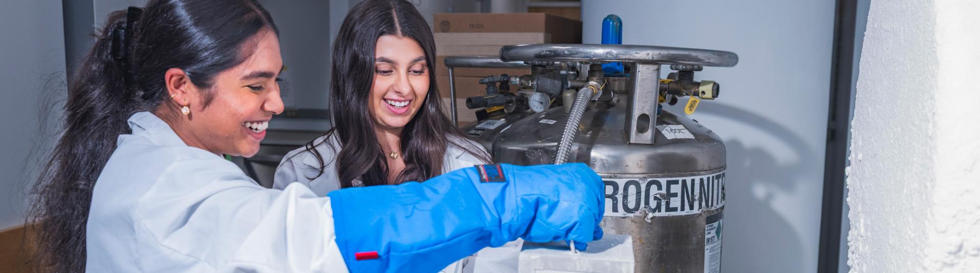 Two students smile as they work on research in cryo chamber during a Genome Sciences lab.