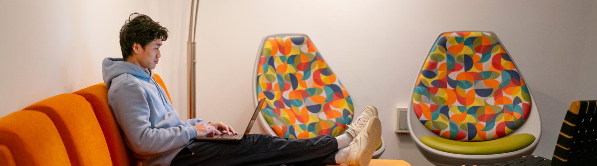 Student sitting on an orange couch on their laptop.