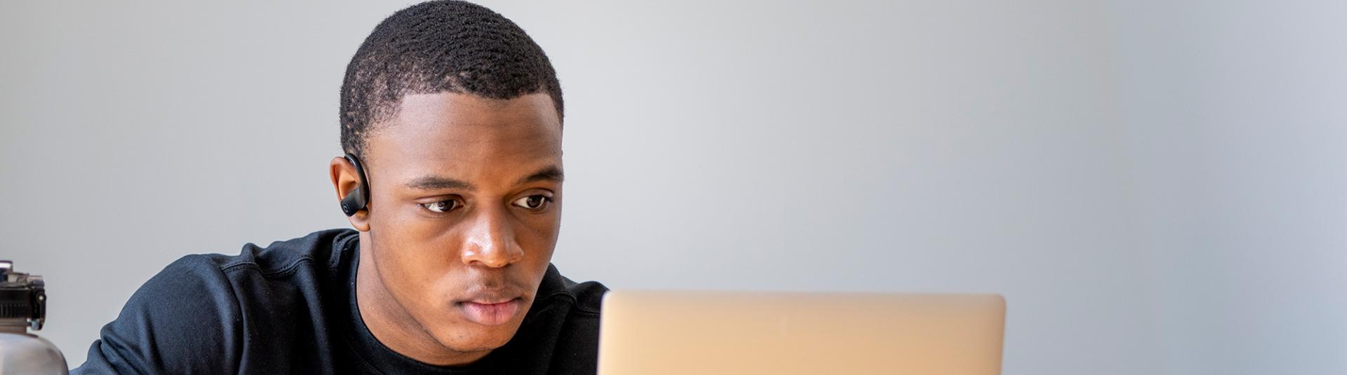 A student sits and focuses intently on a laptop.