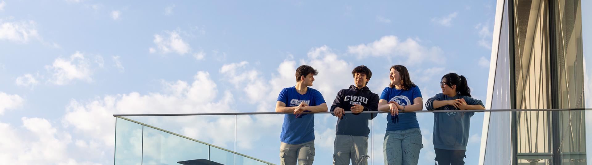 Group of four students standing on a large balcony.