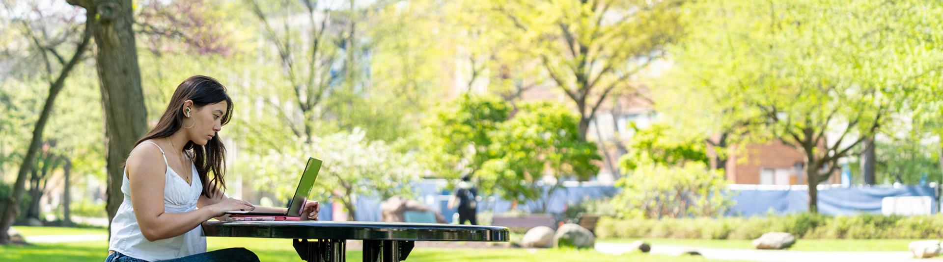A student sits at an outdoor table while working on class work.