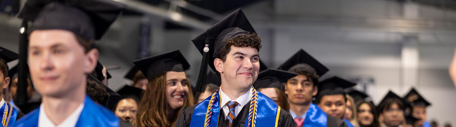Undergraduate students stand in line in graduation regalia to receive their diplomas.