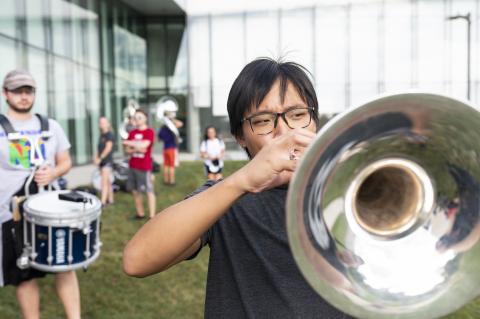 Student plays trumpet outside, drummer in the background