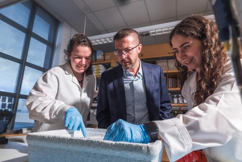 A student smiles as she works with a pipette with two instructors looking on.