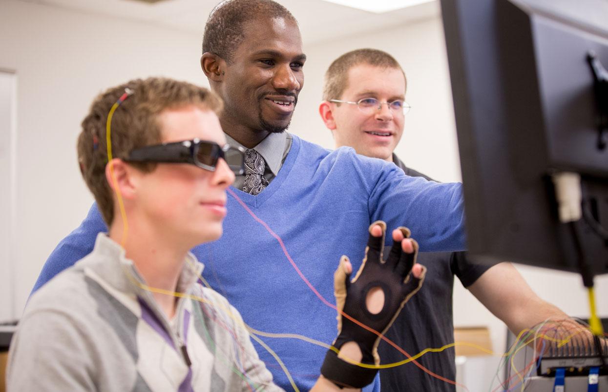 CWRU student wearing a headset and faculty members looking at a computer