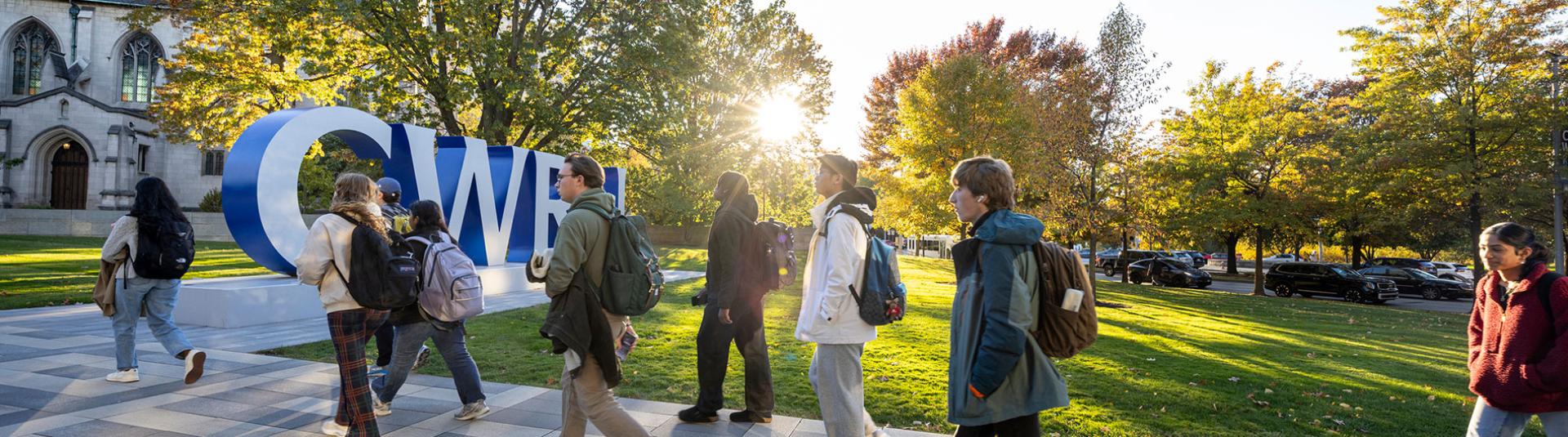 People walking on a walkway through campus in front of CWRU letters
