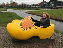 Female student sitting in a wooden shoe while visiting Holland