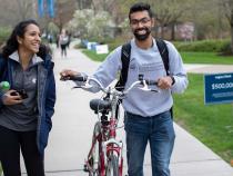 Two students walking and laughing outside, one walking a bike