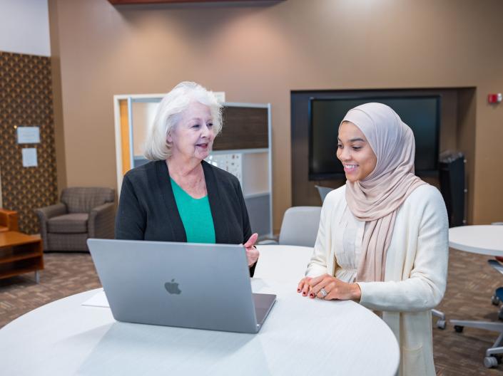 A staff member assists a student with an online assignment in the library.