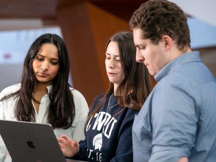 Three individuals stand while discussing an idea on a laptop.
