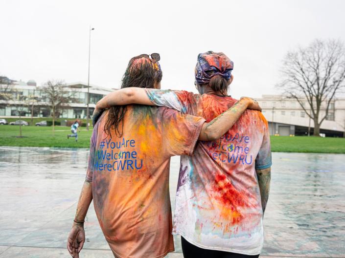 Two students walk away from Holi, covered in paint and arms around each other's shoulders.