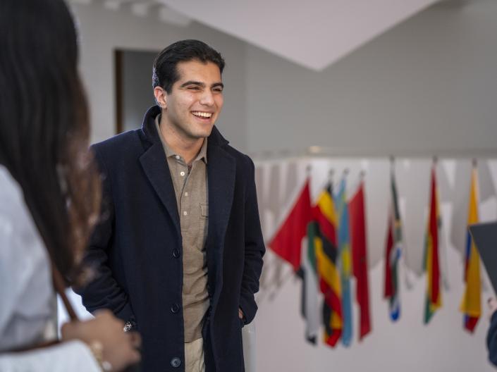 Male student smiling with various country flags in background.