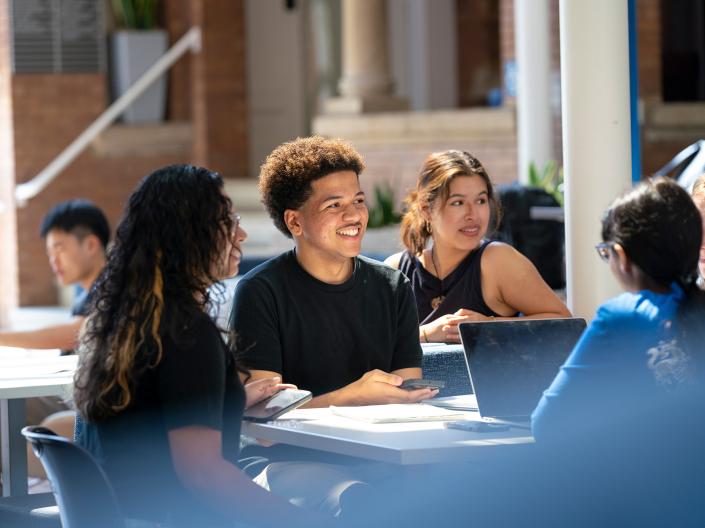 A group of five students sit around a table talking and laughing.