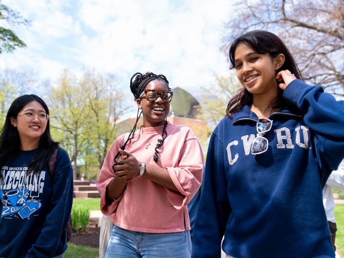 A group of three students laugh together as they walk on campus.
