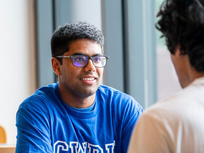 Students sit at a table talking while wearing CWRU shirts.