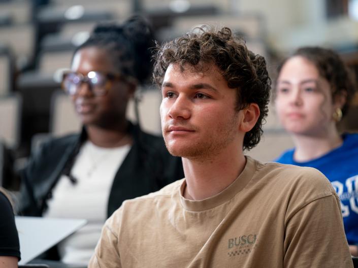 Three students face towards the front of a classroom.
