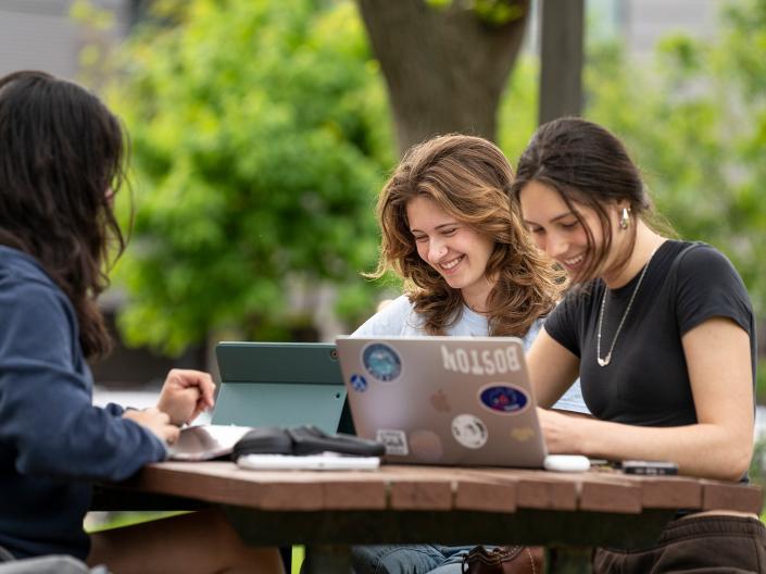 Students working on their laptops at a table outside.