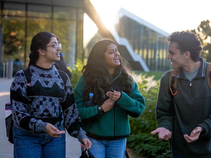 Three students in jackets laugh as they walk together after class.