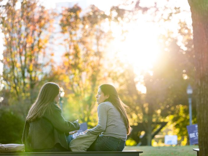 Two students talking on campus with sun in background.