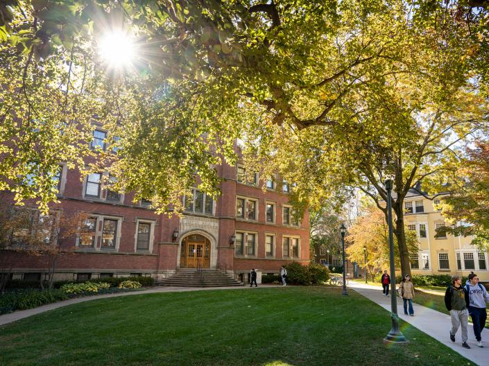 Students walk past buildings in fall lighting.