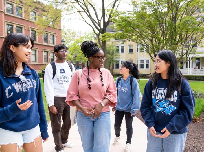 Five students wearing CWRU gear walk and laugh together between classes.