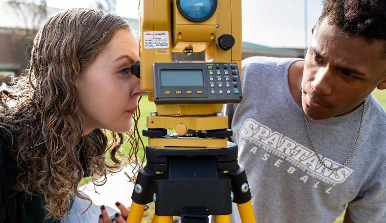 Two students looking through surveying equipment