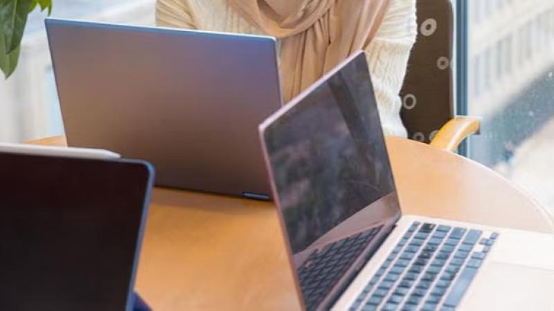 Three people seated at a rounded table with laptop screens open.