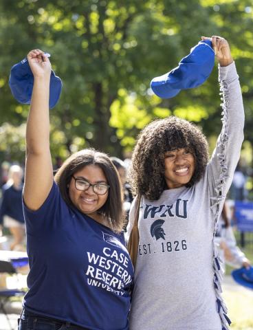 Two undergraduate students smile and throw CWRU-branded hats above their heads.