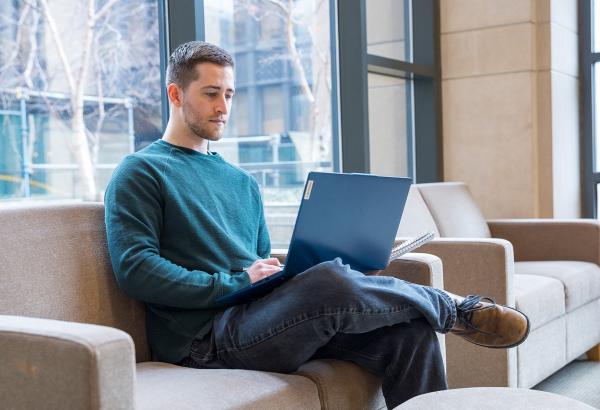 An individual sitting on a couch in the BRB lobby casually working on a computer.