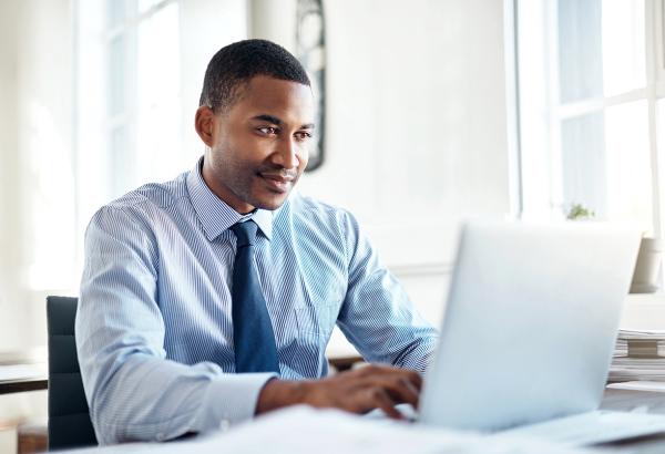 An individual in business attire sits and works on a laptop.