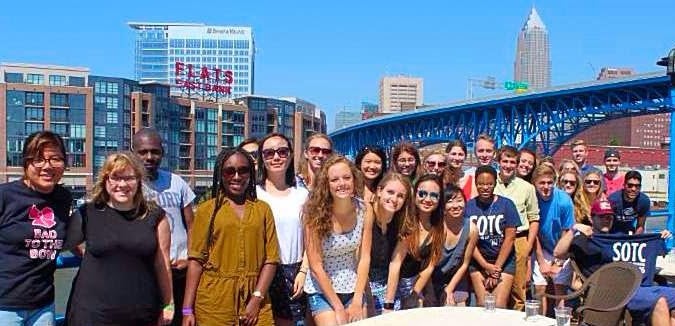 A group picture of Summer on the Cuyahoga, featuring Cleveland-area interns with the Cleveland skyline in the background.