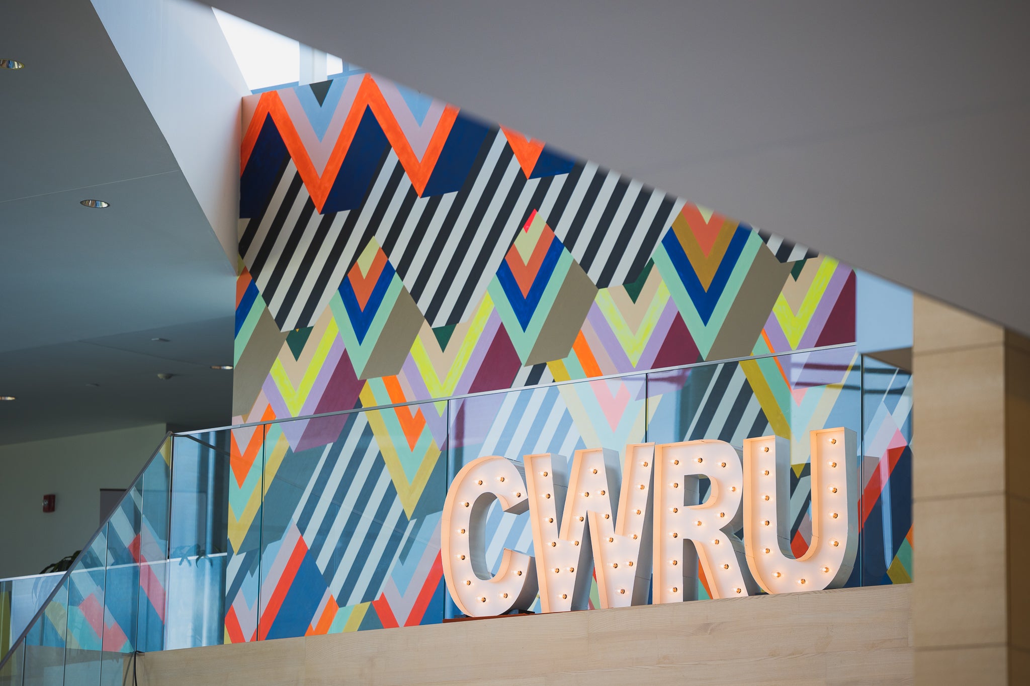 The letters CWRU are spelled in large light-up letters at the top of the stairs in Tinkham Veale University Center, with a colorful patterned background