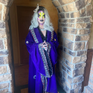 Dr. Lady J stands in full drag makeup and a long, ornate blue robe with a large butterfly clip in her hair.