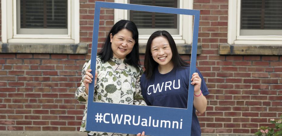 Asian mother and daughter smile at the camera, holding up a frame saying #CWRUalumni