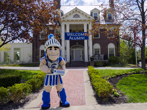 Image of Spartie, on a sunny day standing in front of the Linsalata Alumni Center holding the Ohio CWRU Alumni License Plate