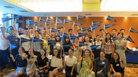 Group of incoming CWRU students, posed and smiling for the camera, waving CWRU pennant flags