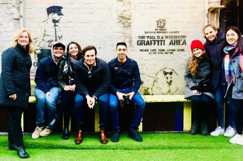 A group of alumni and students in London sit on a public bench during a public art tour.