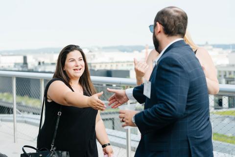 Two alumni reach to shake hands on a rooftop alumni event in Washington D.C.