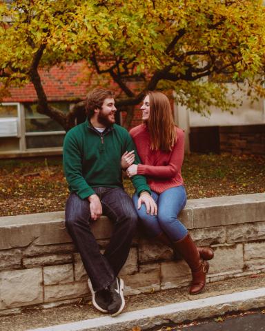 Andrew and Karen Wood sit on a stone wall on campus