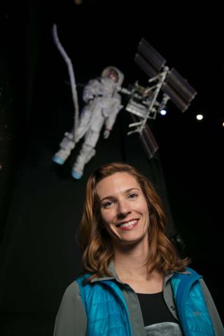 Image of Adele Luta in front of a display of an astronaut working on a satellite. 