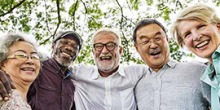 Four smiling, older adults gather around the camera for an outdoor picture