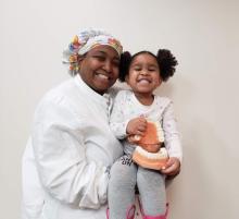 Kari Cunningham, wearing scrubs, holds her niece who holds a dental model; both are smiling