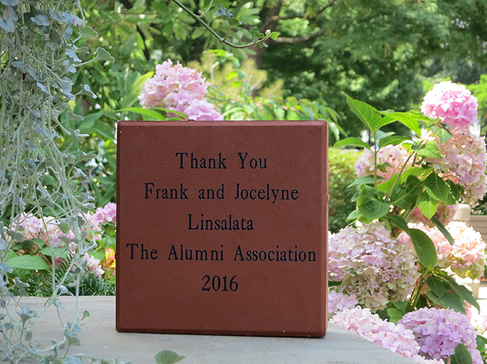 Photo of engraved brick paver, surrounded by spring flowers and greenery
