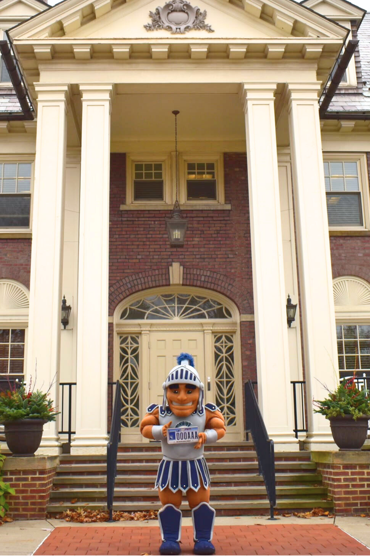 Image of Spartie, on a sunny day standing in front of the Linsalata Alumni Center holding the Ohio CWRU alumni license plate