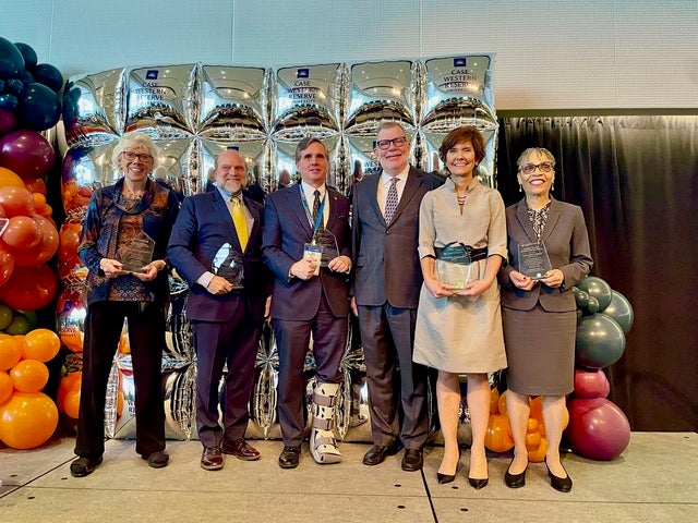 Alumni Association Award recipients and President Eric W. Kaler smile for camera in front of metallic decorative backdrop and balloons