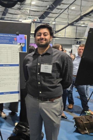Robin Ghotra stands next to a research poster, wearing formal attire